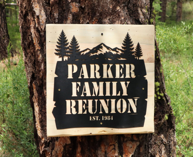 Custom personalized metal sign for the Parker Family Reunion mounted on a handmade wood backboard against a pine tree.