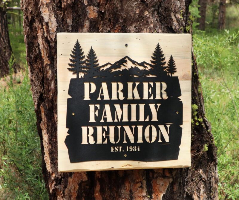 Custom personalized metal sign for the Parker Family Reunion mounted on a handmade wood backboard against a pine tree.